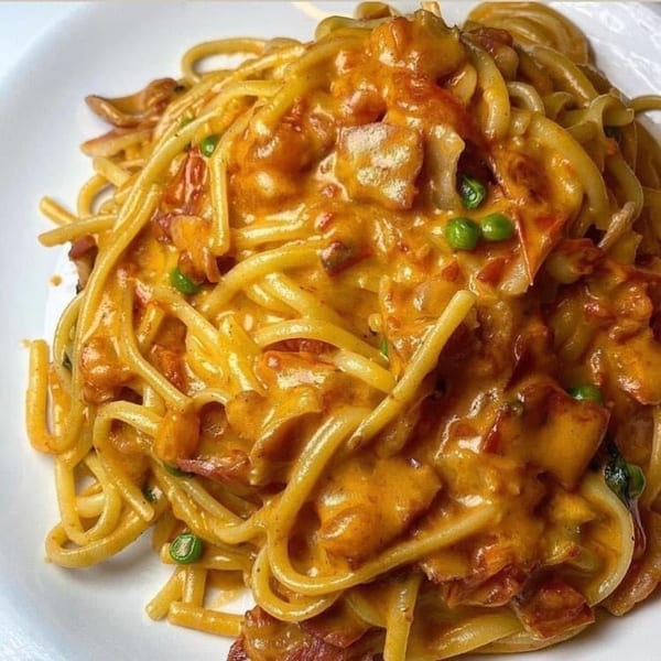 Close-up of Cafe Gia's spaghetti carbonara with peas and bacon in a creamy orange sauce.