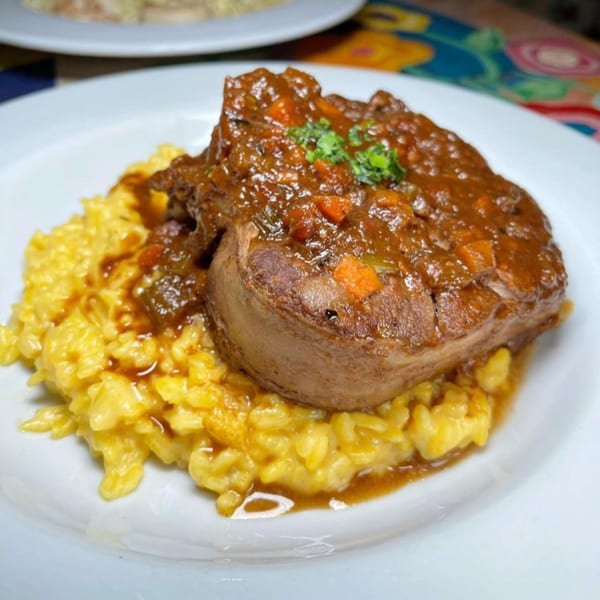 Braised short rib with rich sauce and vegetables, served over creamy yellow risotto on a white plate.