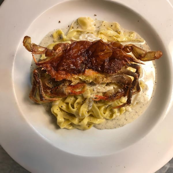 Cafe Gia's fried soft-shell crab atop creamy fettuccine pasta, garnished with black pepper.