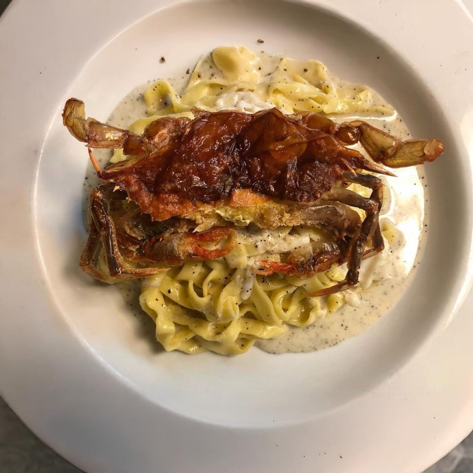 Cafe Gia's fried soft-shell crab atop creamy fettuccine pasta, garnished with black pepper.