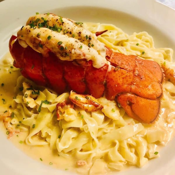 Cafe Gia's lobster tail with creamy fettuccine pasta, garnished with chives on a white plate.
