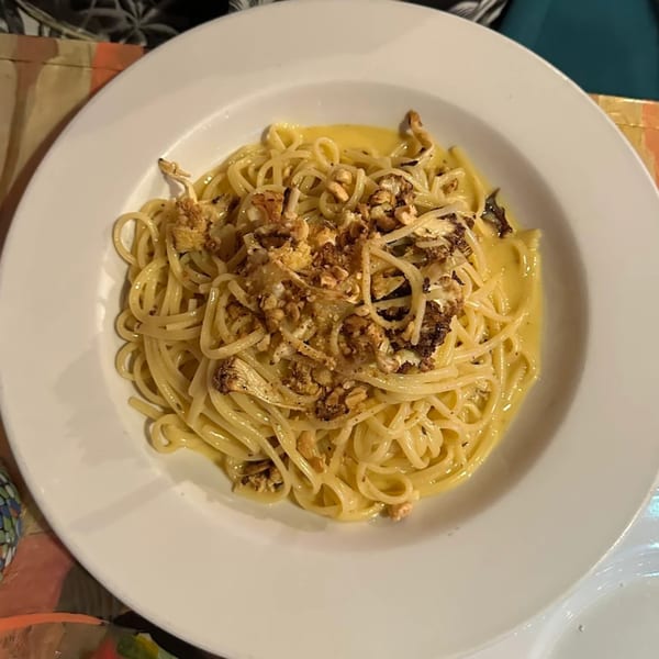 Spaghetti with creamy sauce and roasted cauliflower and nuts in a white bowl.