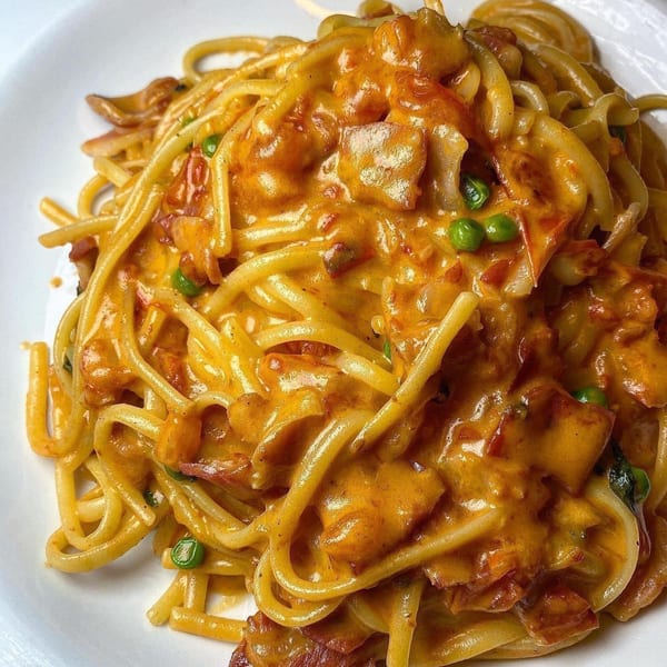 Close-up of Cafe Gia's spaghetti carbonara with a creamy orange sauce, bacon, and green peas.